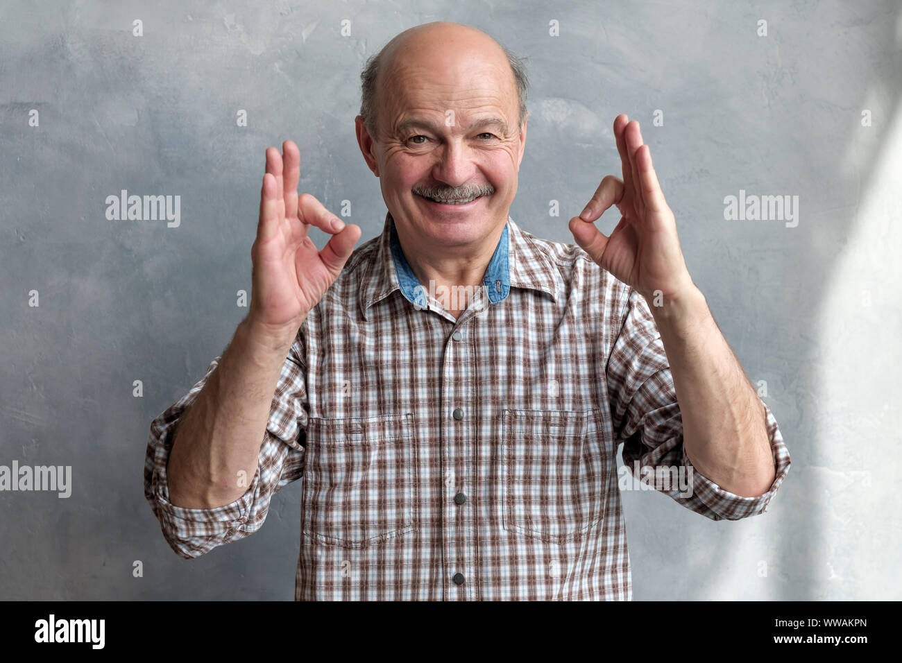 Senior bald hispanic man showing OK sign. Positive facial human emotion Stock Photo