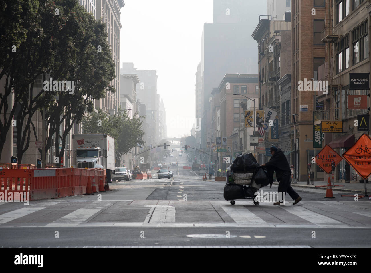San Francisco, California - November 17, 2018: A homeless man pushing a shopping cart is silhouetted as he crosses 2nd Street at the corner of Market. Stock Photo