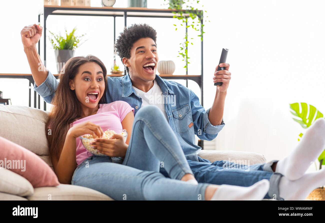 Black Couple Watching Sports On Television And Cheering Stock Photo