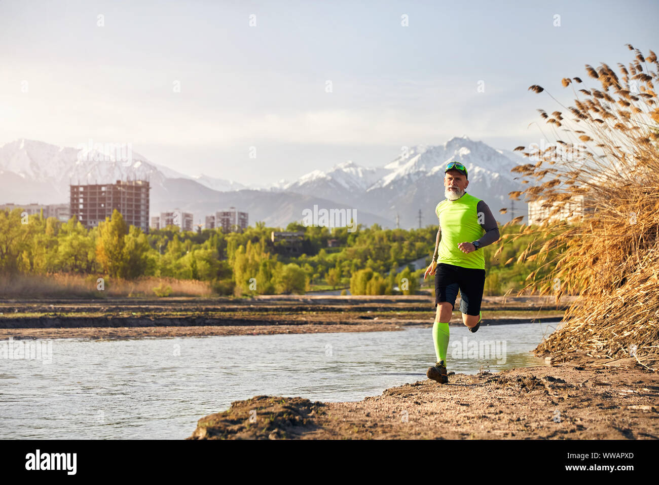 Man with grey beard running near the lake with mountain background in the morning. Healthy lifestyle concept Stock Photo