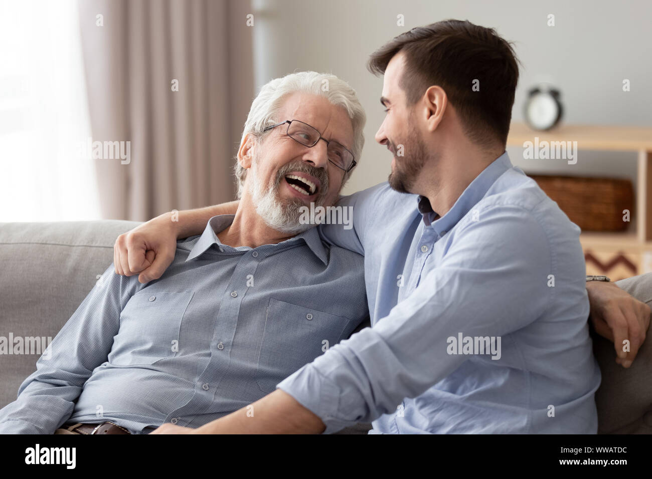 Happy two generations male family laugh talking bonding on sofa Stock Photo
