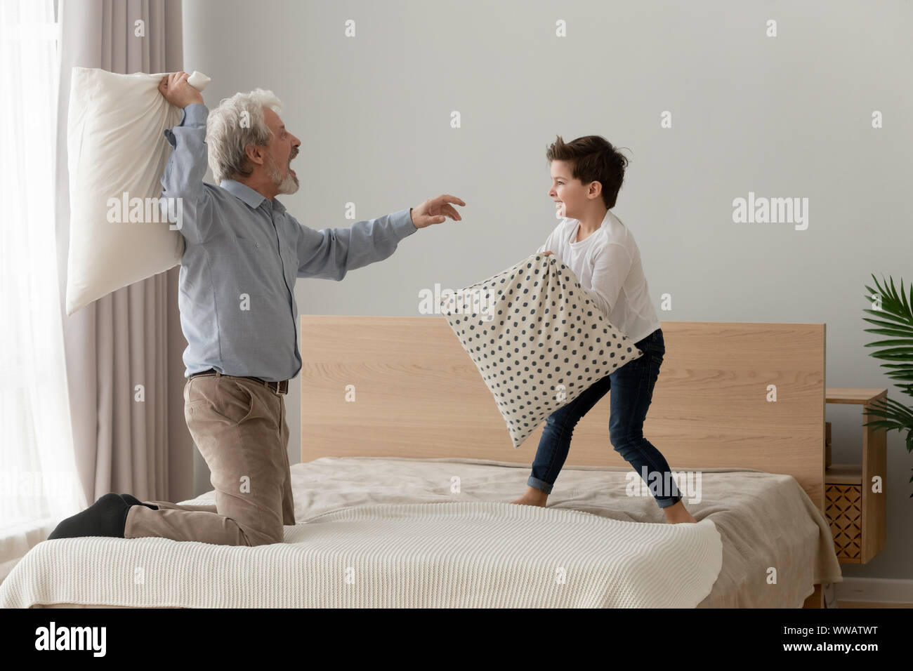 Funny happy grandfather and grandson enjoy pillow fight on bed Stock Photo