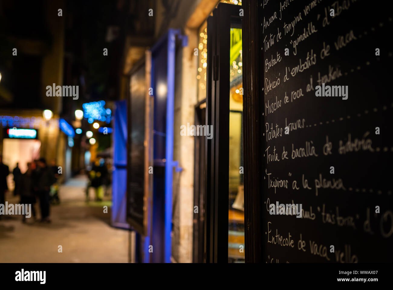 A restaurant menu at night in the Barrio Gotico, with blurred pedestrians in the background. Barcelona, Spain Stock Photo