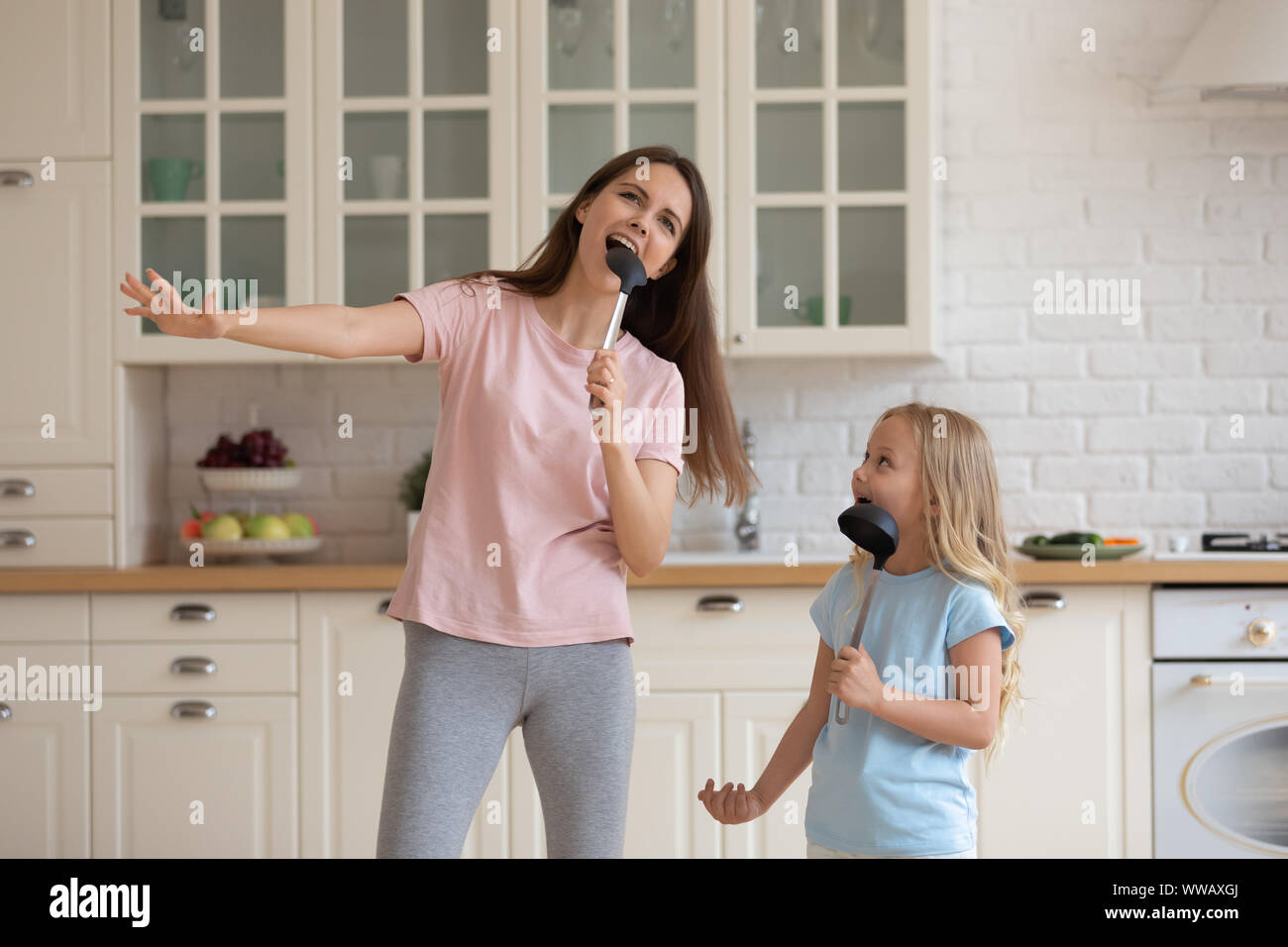 Single mommy with little preschool daughter singing in soup ladles. Stock Photo
