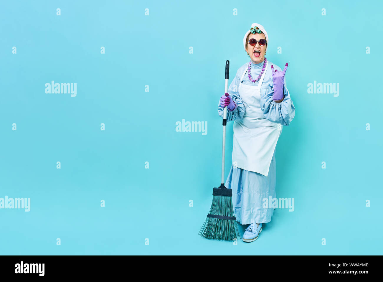 Cleaning Lady Fun. Elderly funky housewife fooling around with a broom. Full body isolated. Comical cleaning lady, old woman funky Stock Photo