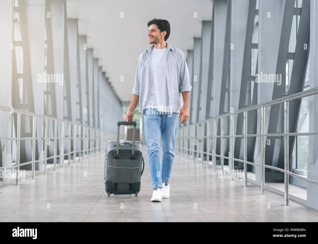 Young man walking in airport walkway with luggage Stock Photo - Alamy