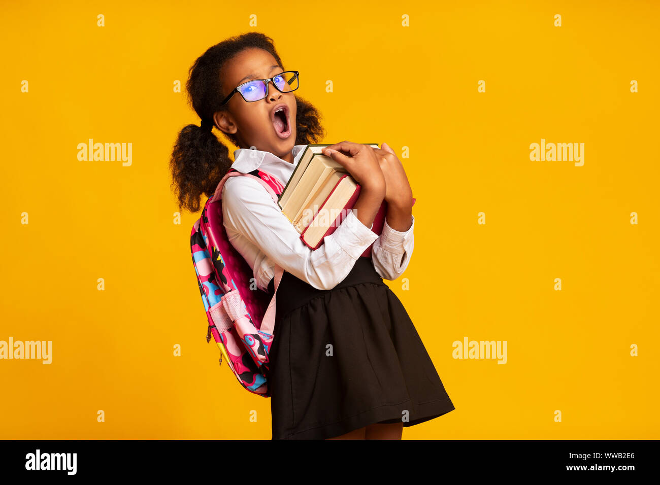 Sleepy African American Schoolgirl Yawning Carrying Books, Yellow Background Stock Photo