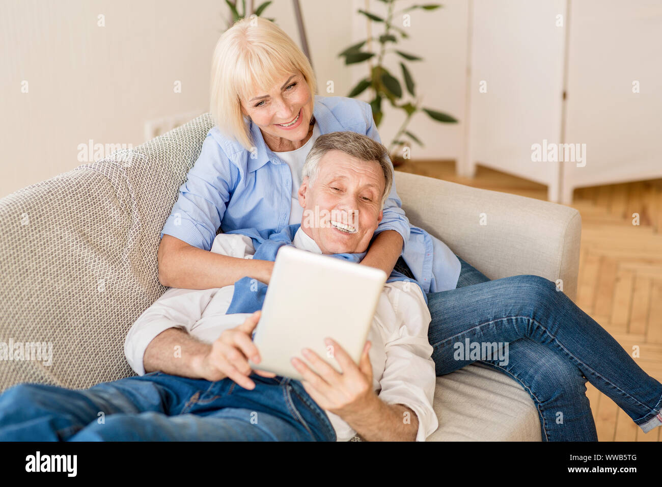 Happy mature spouses using tablet, relaxing on sofa Stock Photo