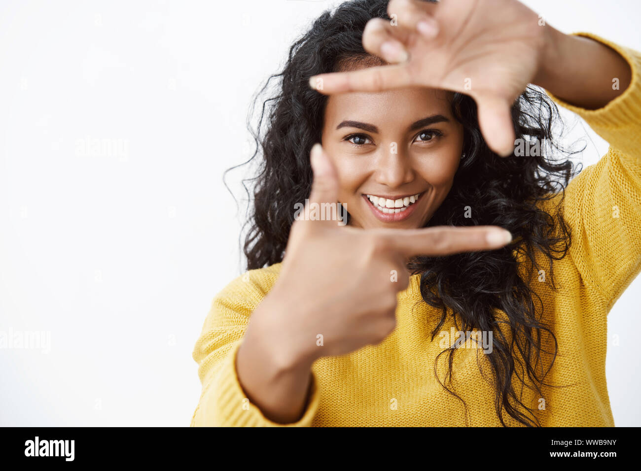 Girl catching every moment. Attractive, cheerful inspired african american woman in yellow sweater searching perfect angle to make shot, show frames Stock Photo