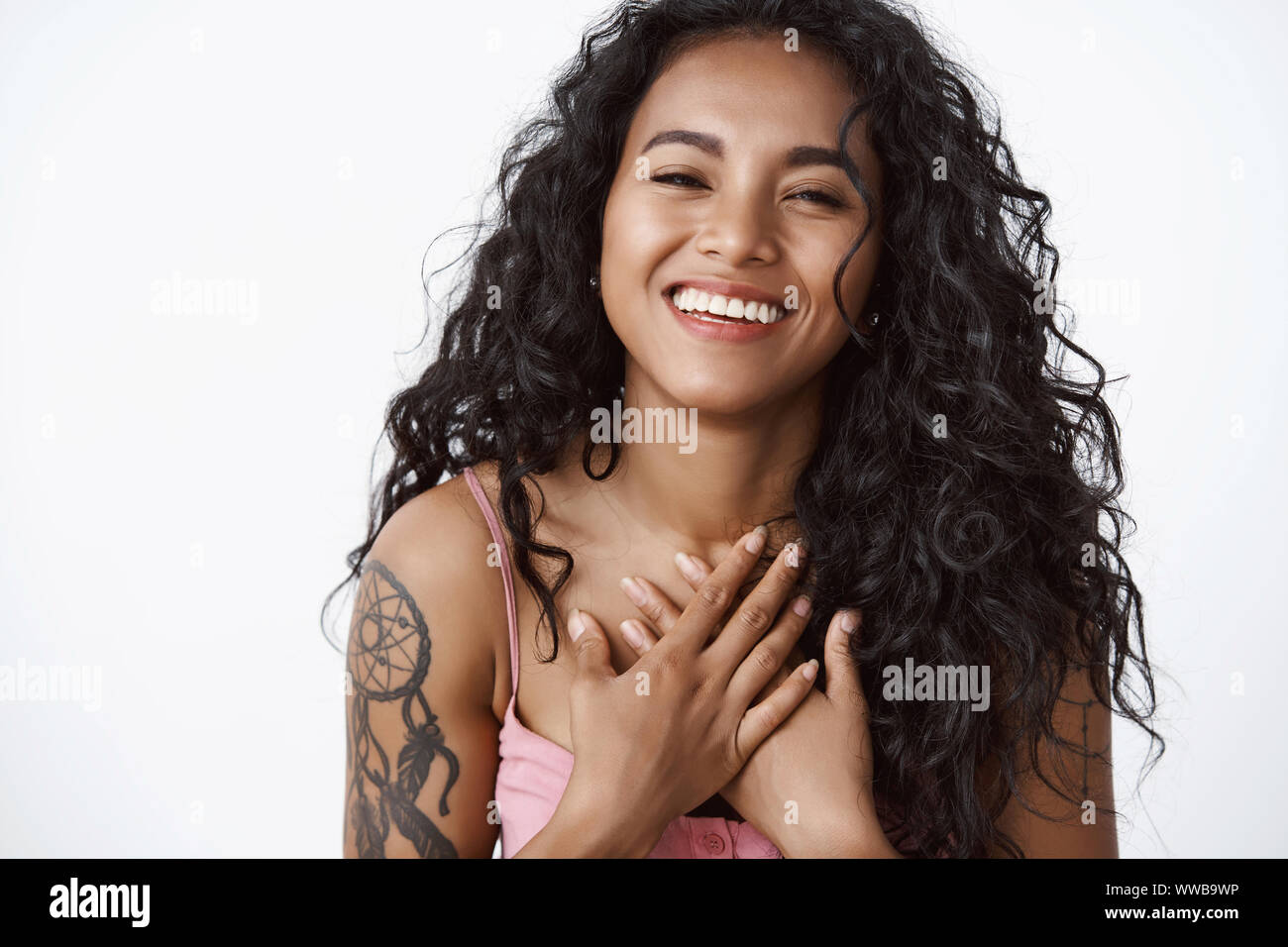 Attractive modern curly-haired african american woman with tattoos, hold hands on chest grateful and touched, laughing and smiling, enjoying touching Stock Photo