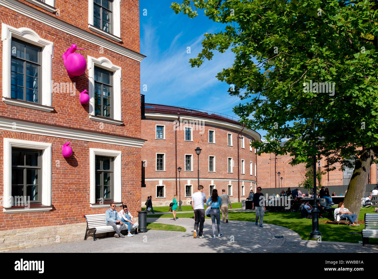 SAINT-PETERSBURG, RUSSIA – JULY 7, 2019: New Holland Island. People near a building with the pink snails on the wall by Cracking Art Stock Photo