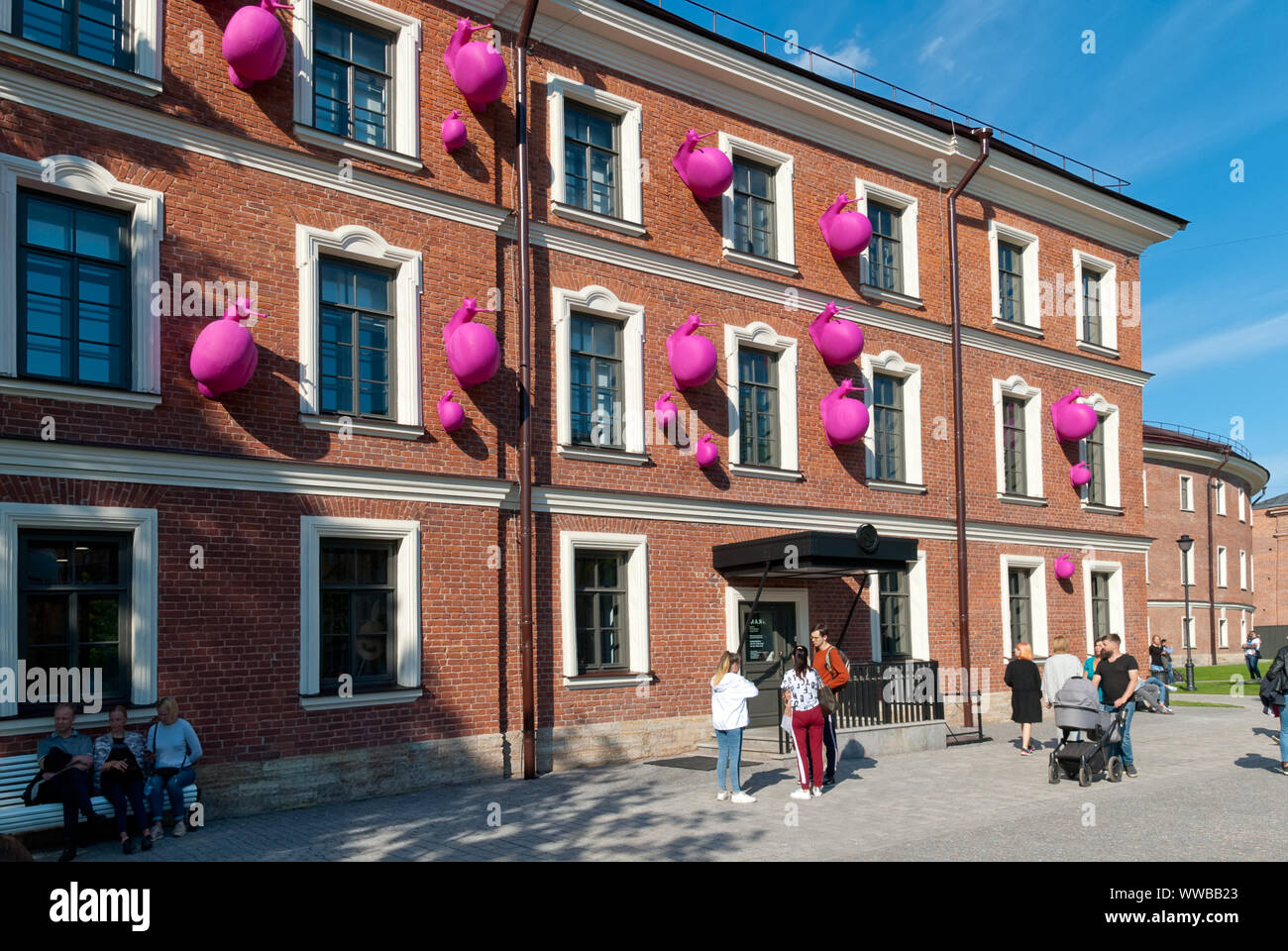 SAINT-PETERSBURG, RUSSIA – JULY 7, 2019: New Holland Island. People near a building with the pink snails on the wall by Cracking Art Stock Photo