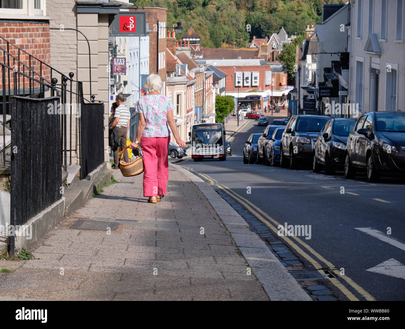 Woman with a basket walking downhill High Street, Lewes towards to city center, while bus heads to other way. Lewes, UK, September 2019 Stock Photo