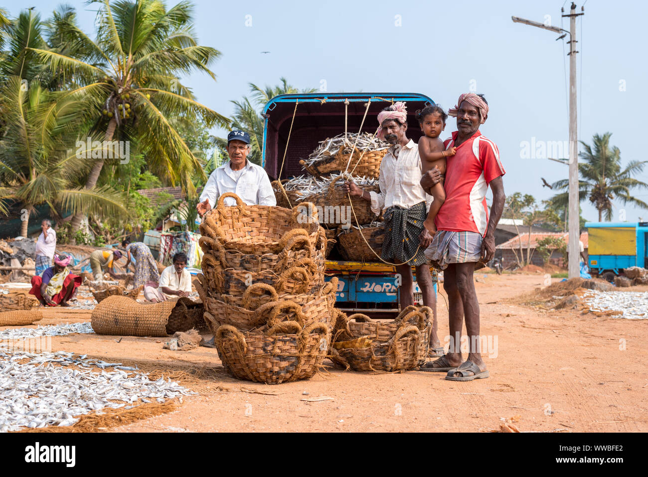 Mangalore, India: Group of men with a baby girl pose beside coir baskets with dried fish. Stock Photo