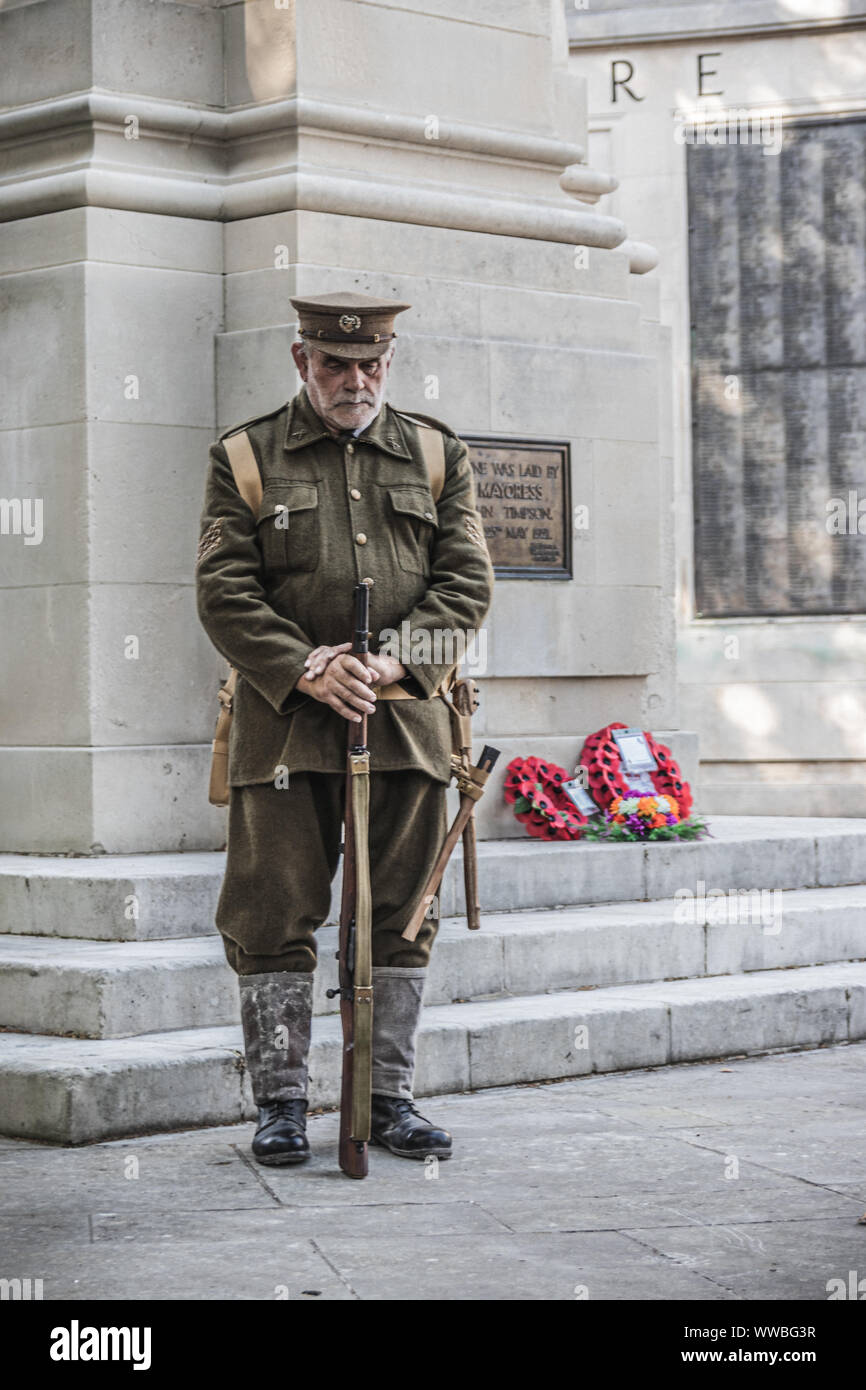 A man in World war one soldiers uniform standing next to a British war memorial with red poppy wreaths laid on it Stock Photo