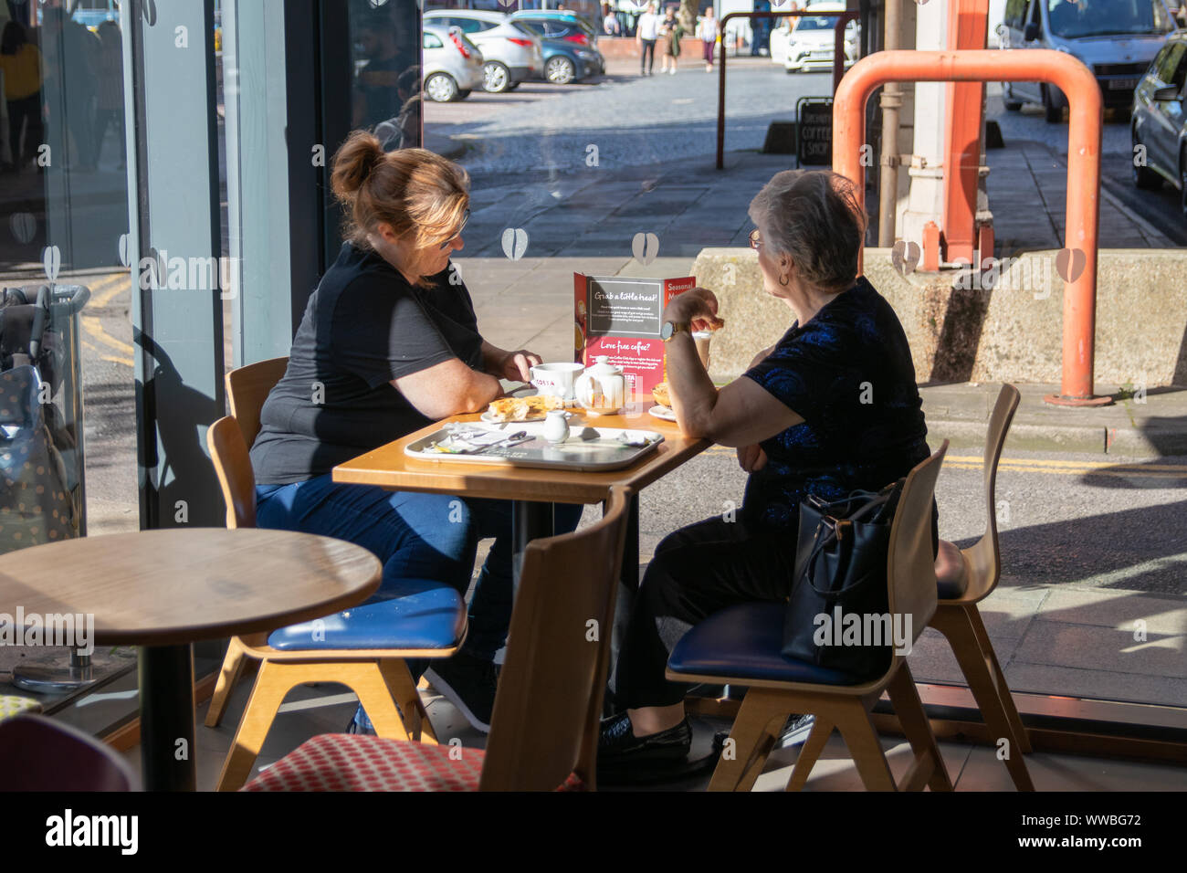 A middle aged woman and her elderly mother talking whilst having a coffee in a coffee shop Stock
