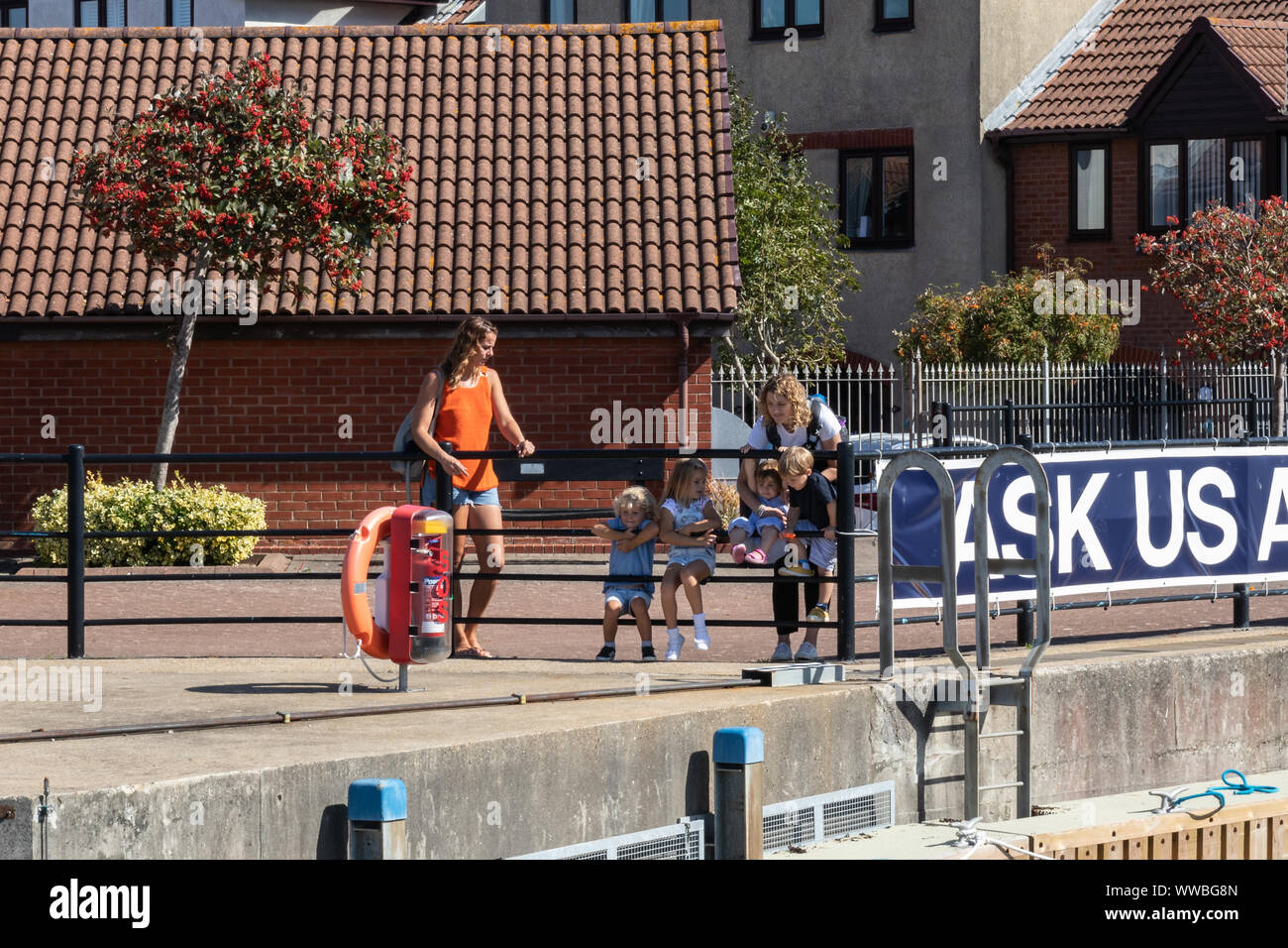 A family looking over railings at a lock watching boats enter a harbour Stock Photo
