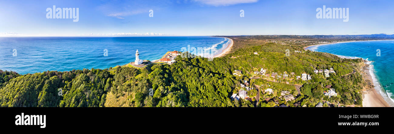 WHite stone Byron Bay lighthouse on the top of green wood covered headland in wide aerial panorama overlooking Byron Bay town and coast with beaches u Stock Photo