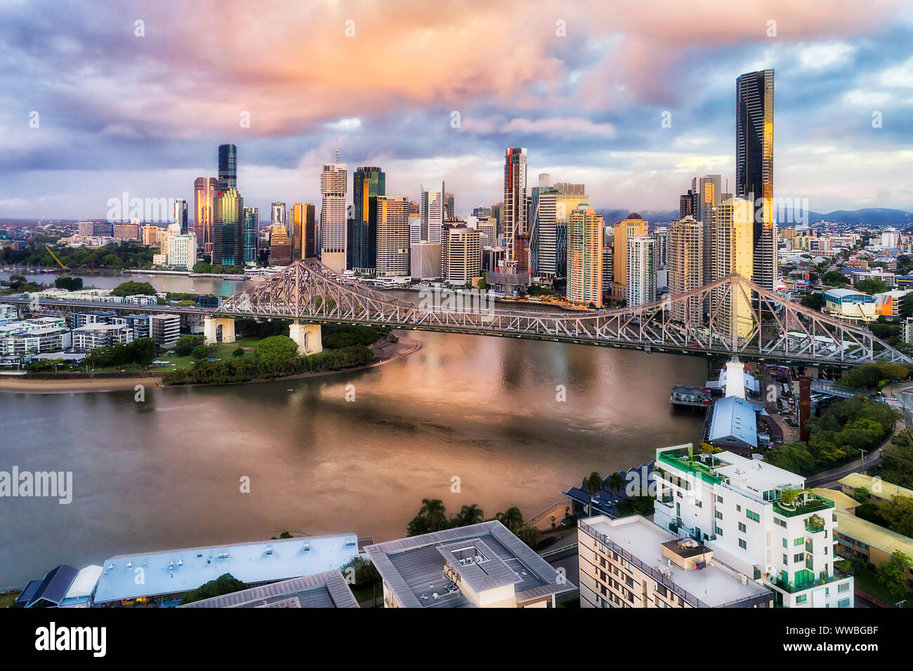 Story bridge in Brisbane city over Brisbane river in front of high-rise business towers and apartment buildings at sunrise in elevated aerial view. Stock Photo