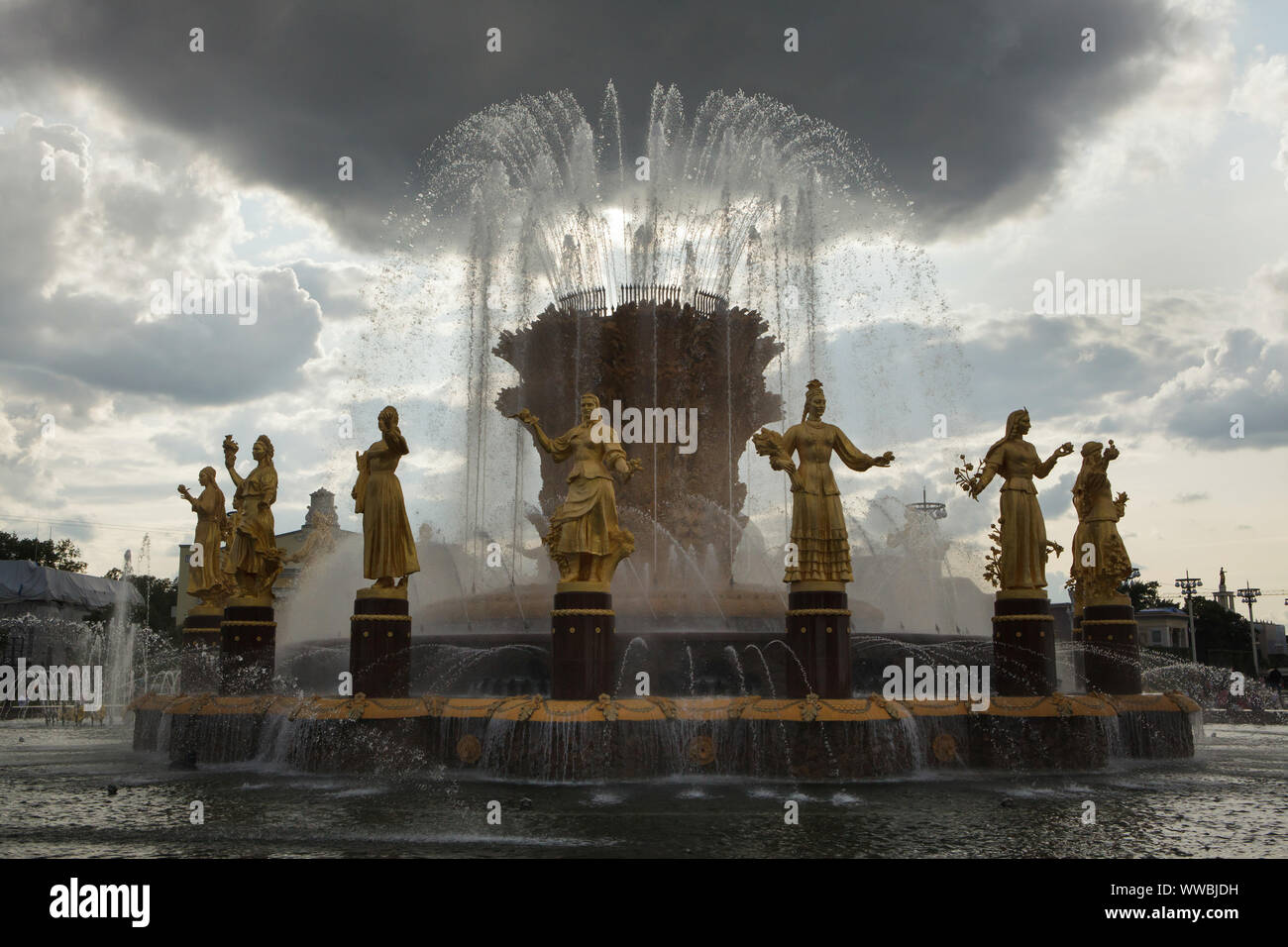 Friendship of Nations (Friendship of Peoples) Fountain on the main square in the VDNH exhibition ground (Exhibition of Achievements of National Economy) in Moscow, Russia. The fountain designed by Soviet architect Konstantin Topuridze decorated with sixteen gilded statues of the nations of the Soviet Union by Soviet sculptors Zinaida Bazehenova, Alexey Teneta, Iosif Chaykov, Zoya Ryleyeva and others was built in 1954. The fountain is also known as the Golden Sheaf. Stock Photo