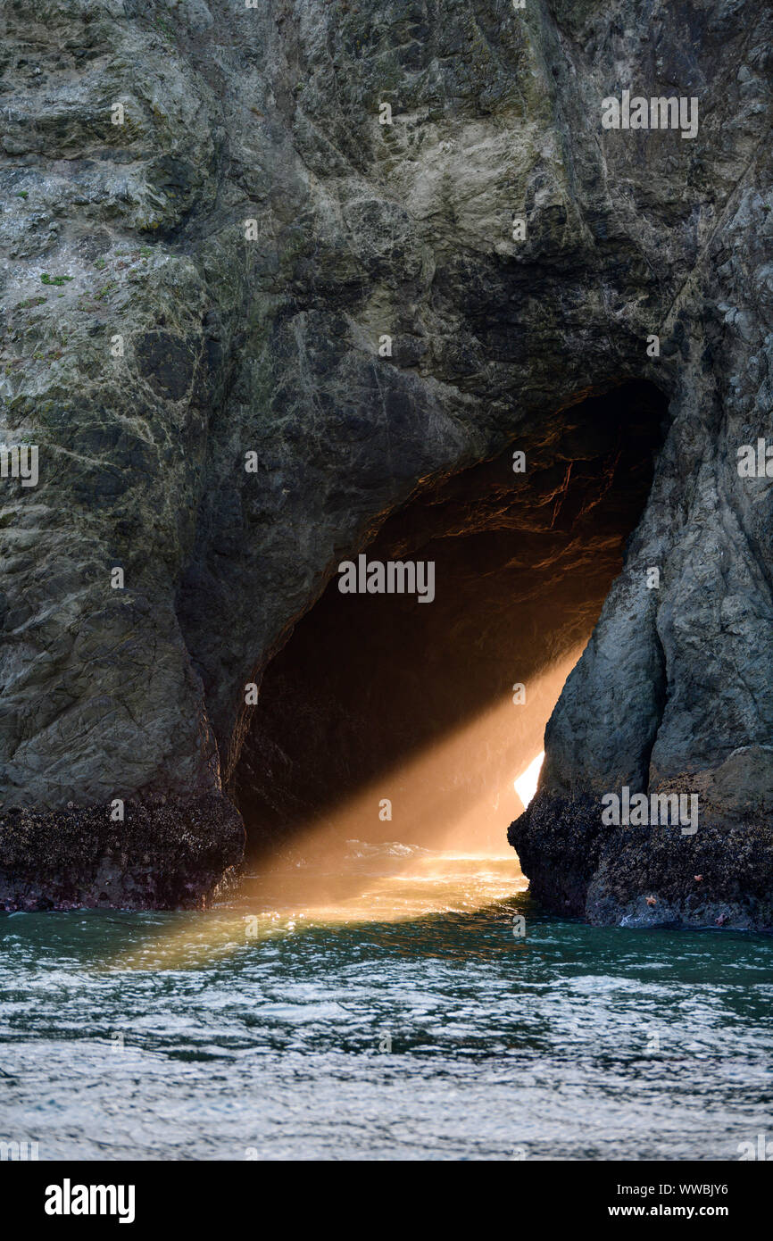 The sun sets through Harris Creek State Park sea arch just north of Brookings, Oregon, North America along the Pacific coast. Stock Photo