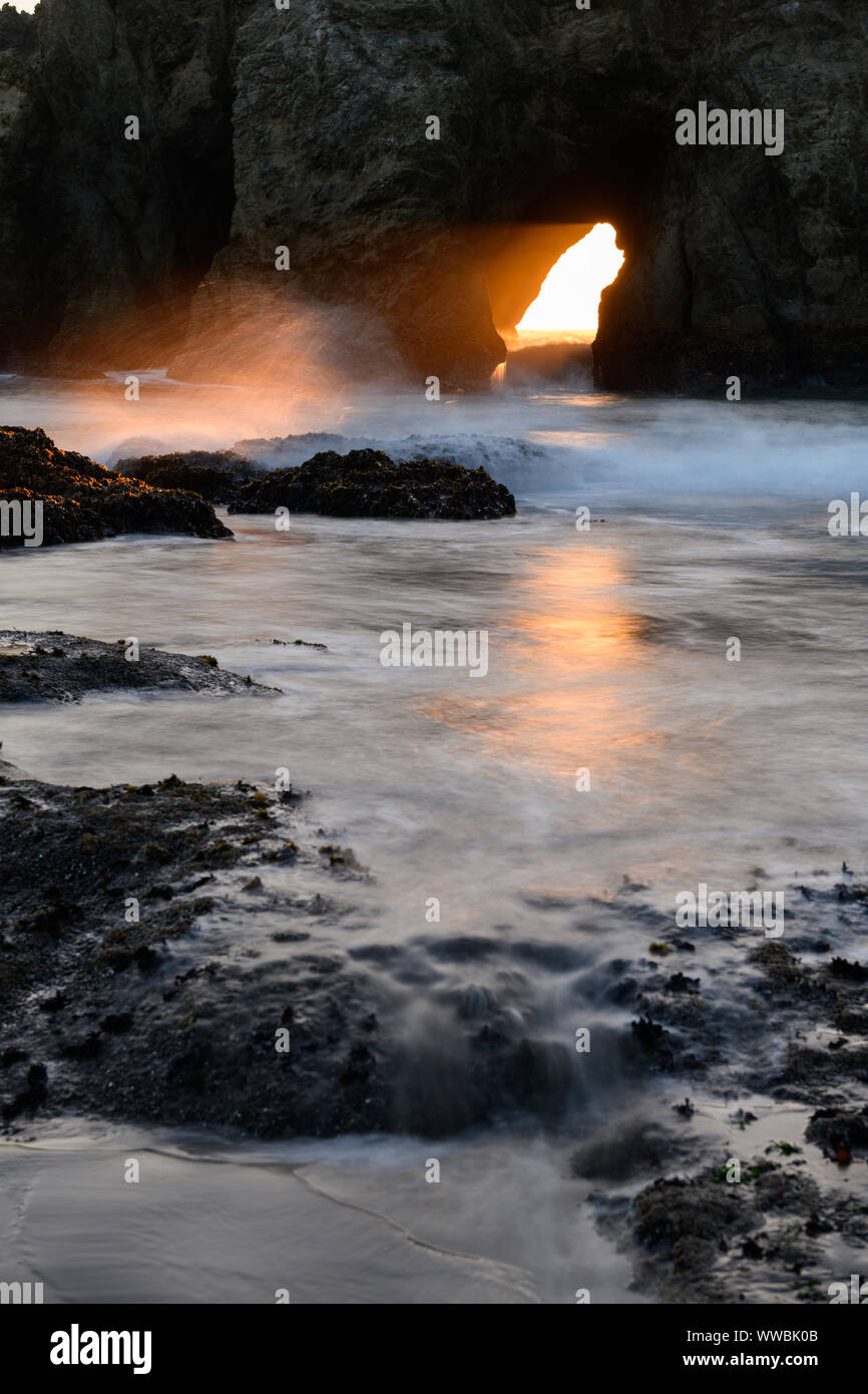 The sun sets through Harris Creek State Park sea arch just north of Brookings, Oregon, North America along the Pacific coast. Stock Photo