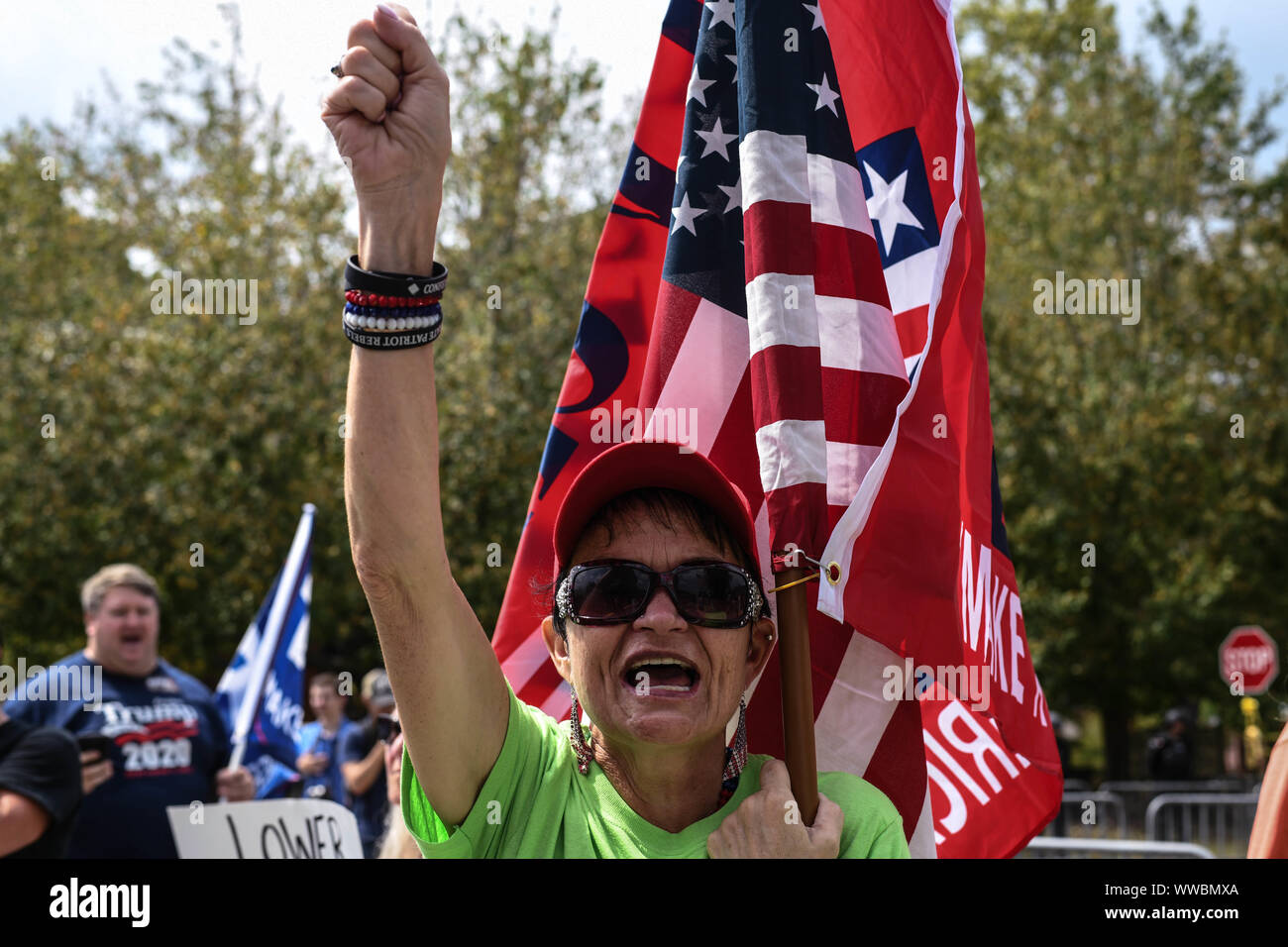 Dahlonega, Georgia, USA. 14th Sep, 2019. A woman waves an American flag and a pro-Trump flag as she says the Pledge of Allegiance during a rally organized by longtime white nationalist leader Chester Doles in Dahlonega, Georgia on Saturday. Doles billed the event as an 'American Patriot Rally'' to honor Trump and many of those who attended bore swastika tattoos and other symbols of white supremacy. Hundreds of law enforcement officers outnumbered the rally participants and counter protesters. Credit: Miguel Juarez Lugo/ZUMA Wire/Alamy Live News Stock Photo