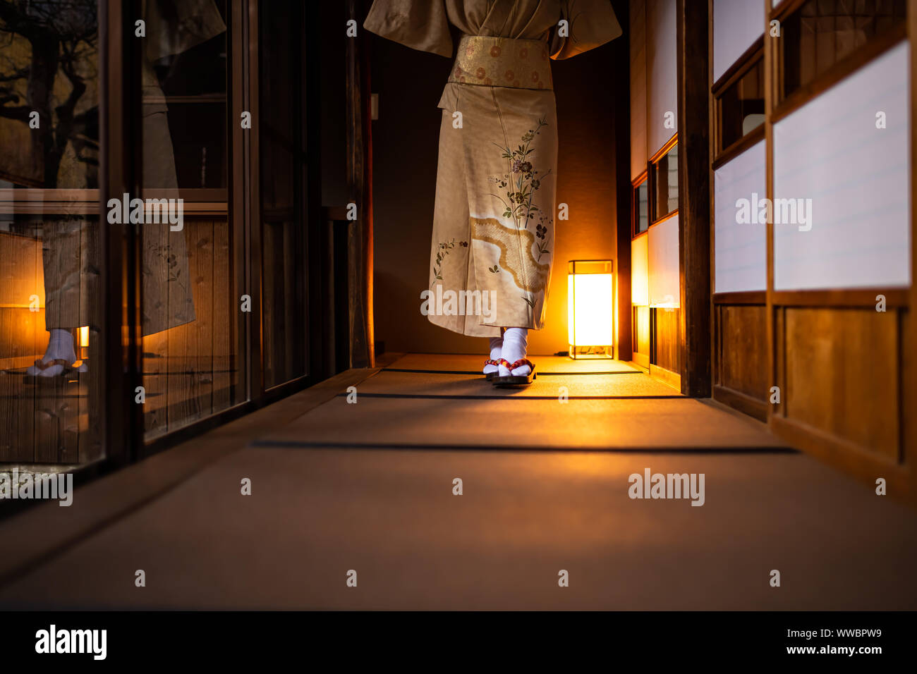 Traditional Japanese house ryokan, tatami mat floor and shoji sliding paper doors, woman in kimono and geta shoes tabi socks walking in corridor hall Stock Photo