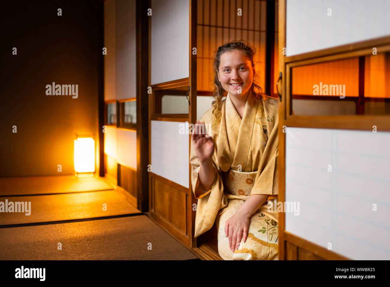 Traditional japanese house or ryokan with gaijin caucasian woman in kimono and tabi socks waving hands from opened shoji sliding paper doors sitting o Stock Photo