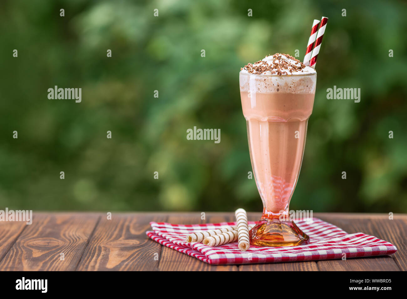 chocolate milkshake in glass with whipped cream and wafer rolls on wooden table outdoors Stock Photo