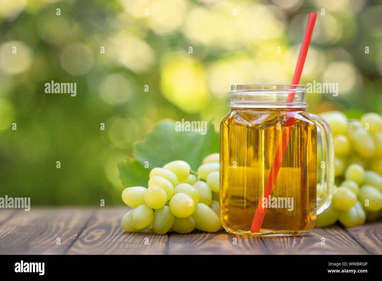 fresh grape juice in glass mason jar with ripe bunch of green berries on wooden table outdoors ...