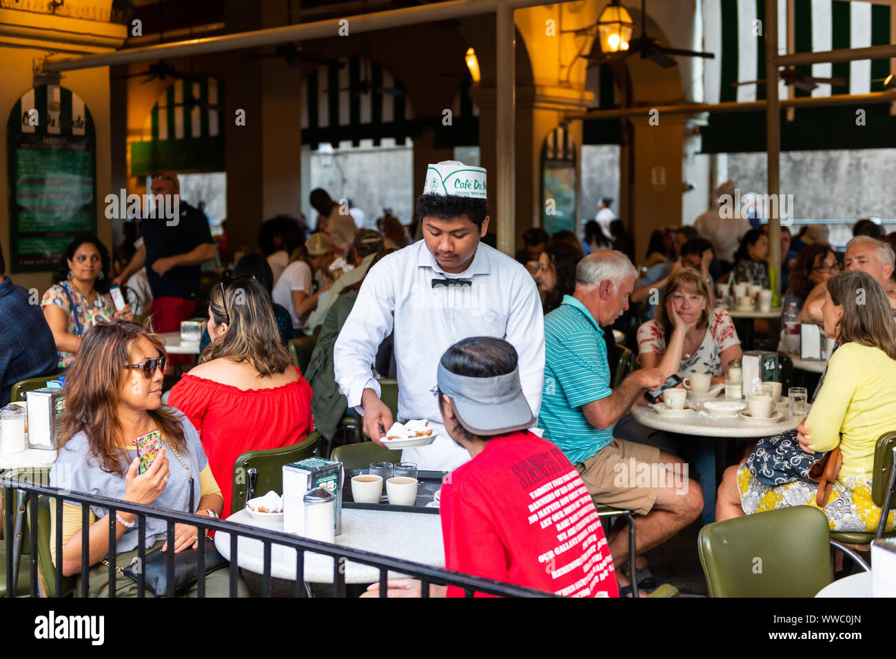 New Orleans, USA - April 22, 2018: People in famous Cafe Du Monde restaurant eating beignet powdered sugar donuts, drinking chicory coffee served by w Stock Photo