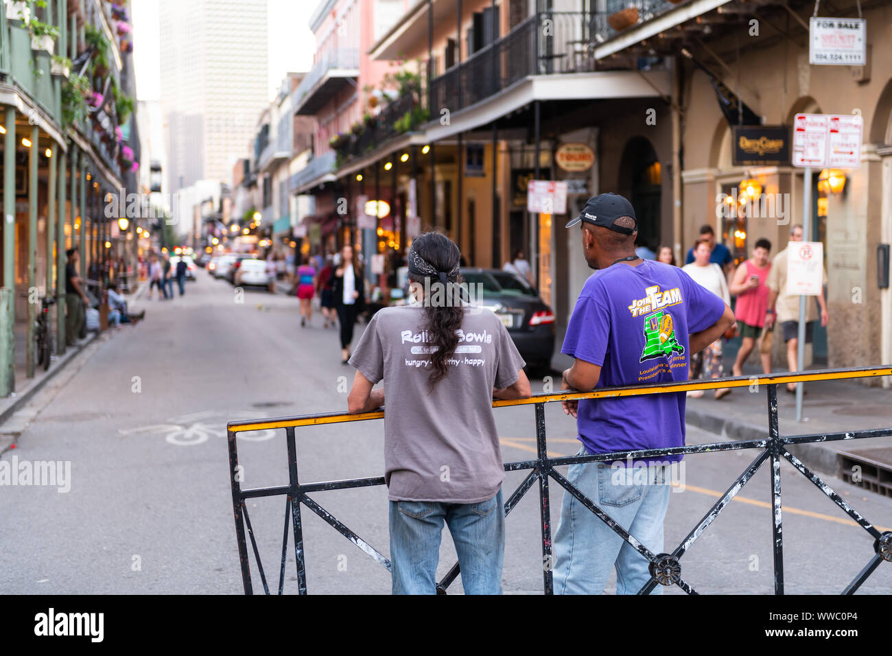 New Orleans, USA - April 22, 2018: Back of two local men standing on Bourbon street road in evening with people walking in blurry background of Louisi Stock Photo