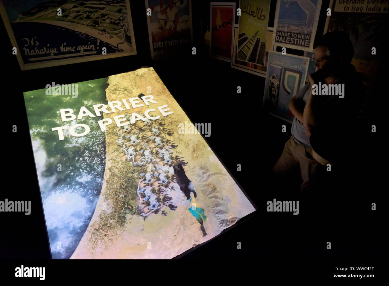 A tourist watches an audio visual installation about the history of the Israel/Palestine conflict at the small museum inside the Walled Off Hotel by acclaimed artist Banksy built alongside the Israeli West Bank barrier in the Palestinian city of Bethlehem in central West Bank, Palestinian Territories Israel Stock Photo