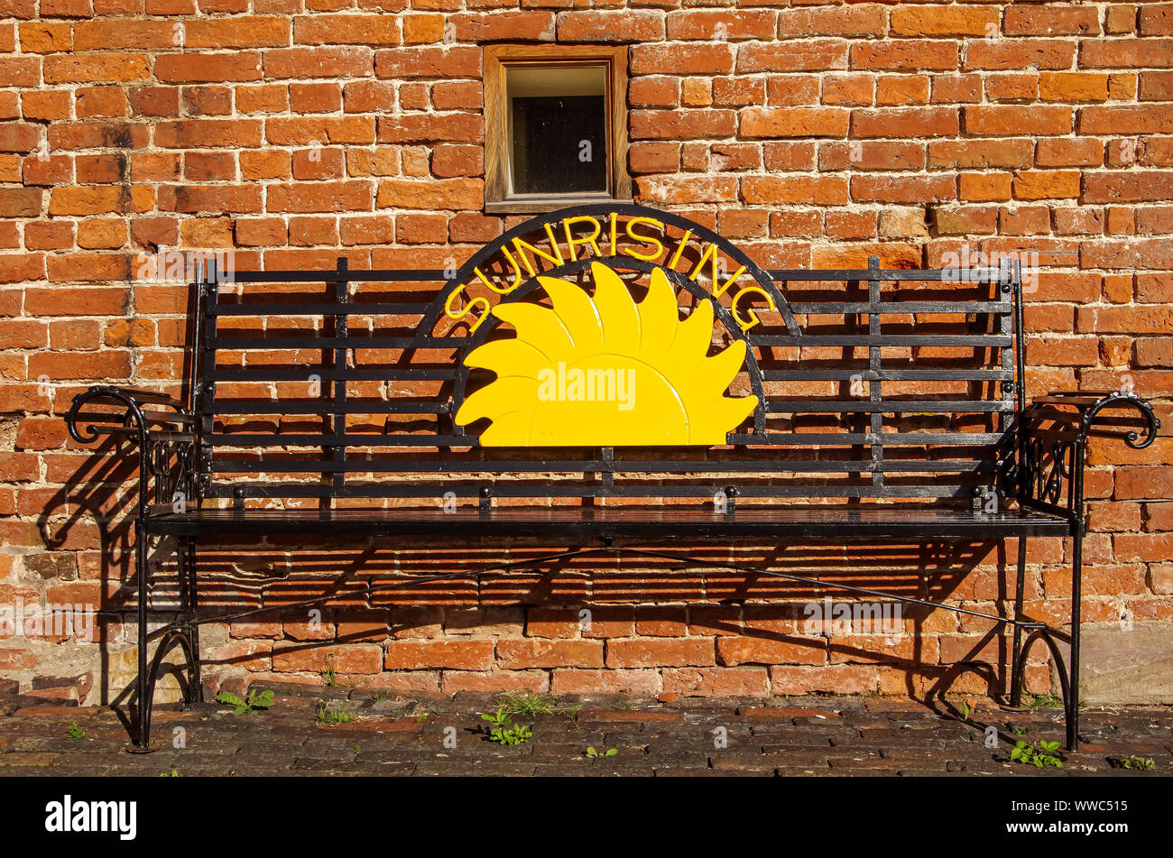 Sunrising sign in metal bench in front of red brick wall Stock Photo