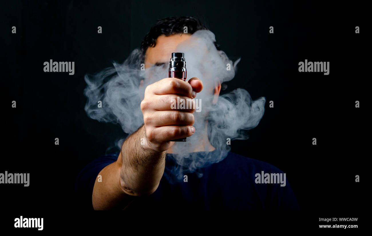 hand holding vape e-cigarette or electronic cigarette with white smoke over  a black background Stock Photo