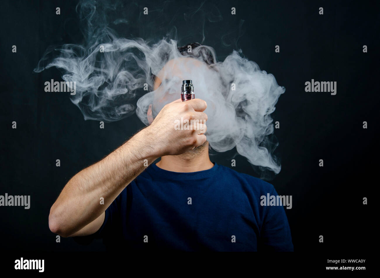 101 vape & smoke shop hand holding vape e-cigarette or electronic cigarette with white smoke over  a black background Stock Photo