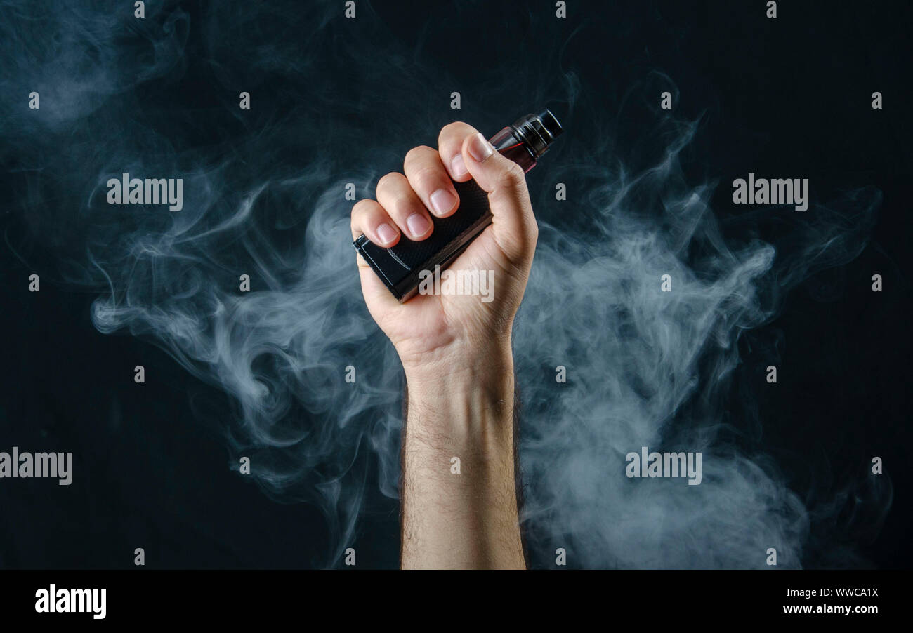 holding in vape smoke hand holding vape e-cigarette or electronic cigarette with white smoke over  a black background Stock Photo