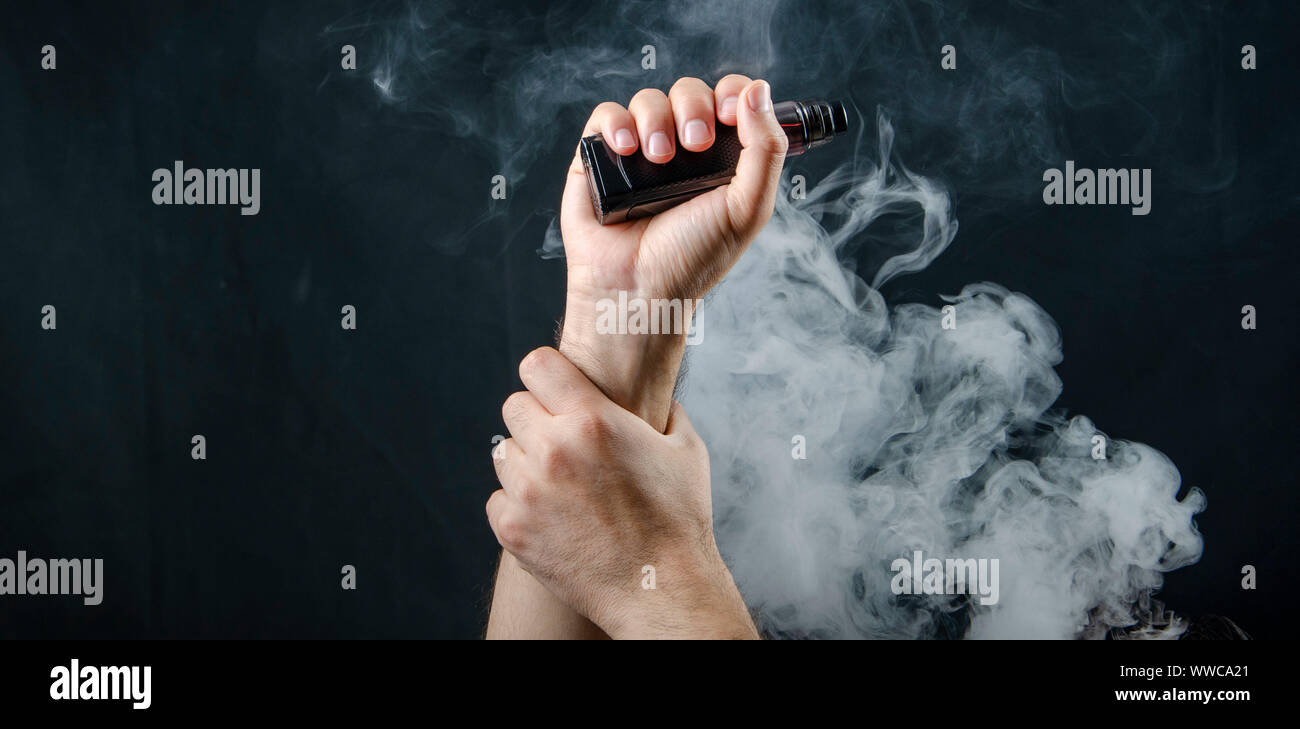 heavy clouds smoke and vape shop upland hand holding vape e-cigarette or electronic cigarette with white smoke over  a black background Stock Photo