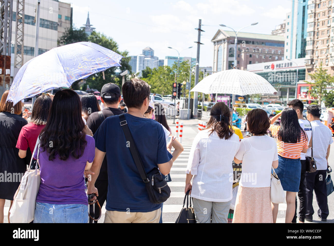 Beijing, China - August 17, 2019. A crowd of Chinese people are waiting for a green light. Chinese women hiding from the sun under umbrella. Stock Photo