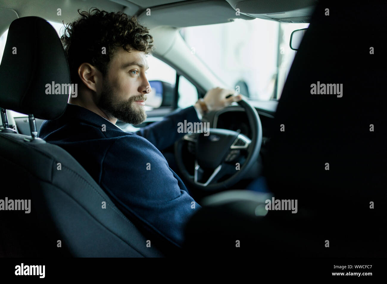 Rear view of man sitting in new car in showroom. Stock Photo