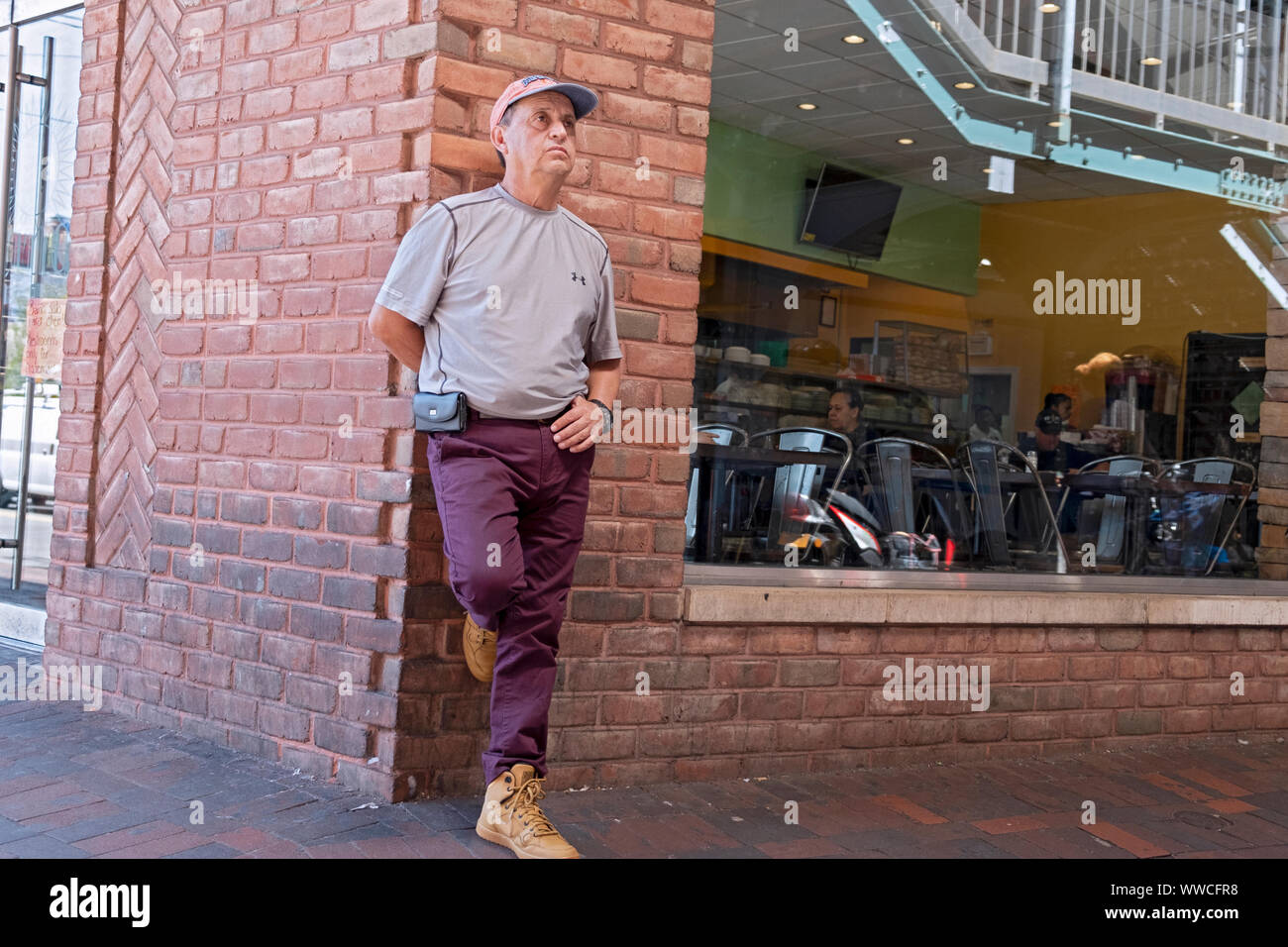 A middle aged man lost in thought while leaning up against a building. Under the elevated subway in Jackson Heights, Queens, New York City. Stock Photo