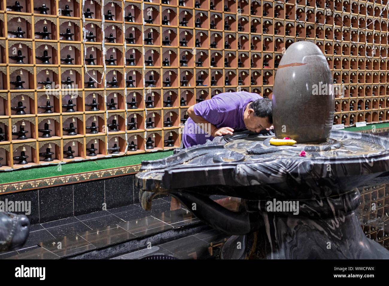 A devout Hindu man bows in prayer at a Shiva Lingam inside a temple in Woodside, Queens, New York City. Stock Photo