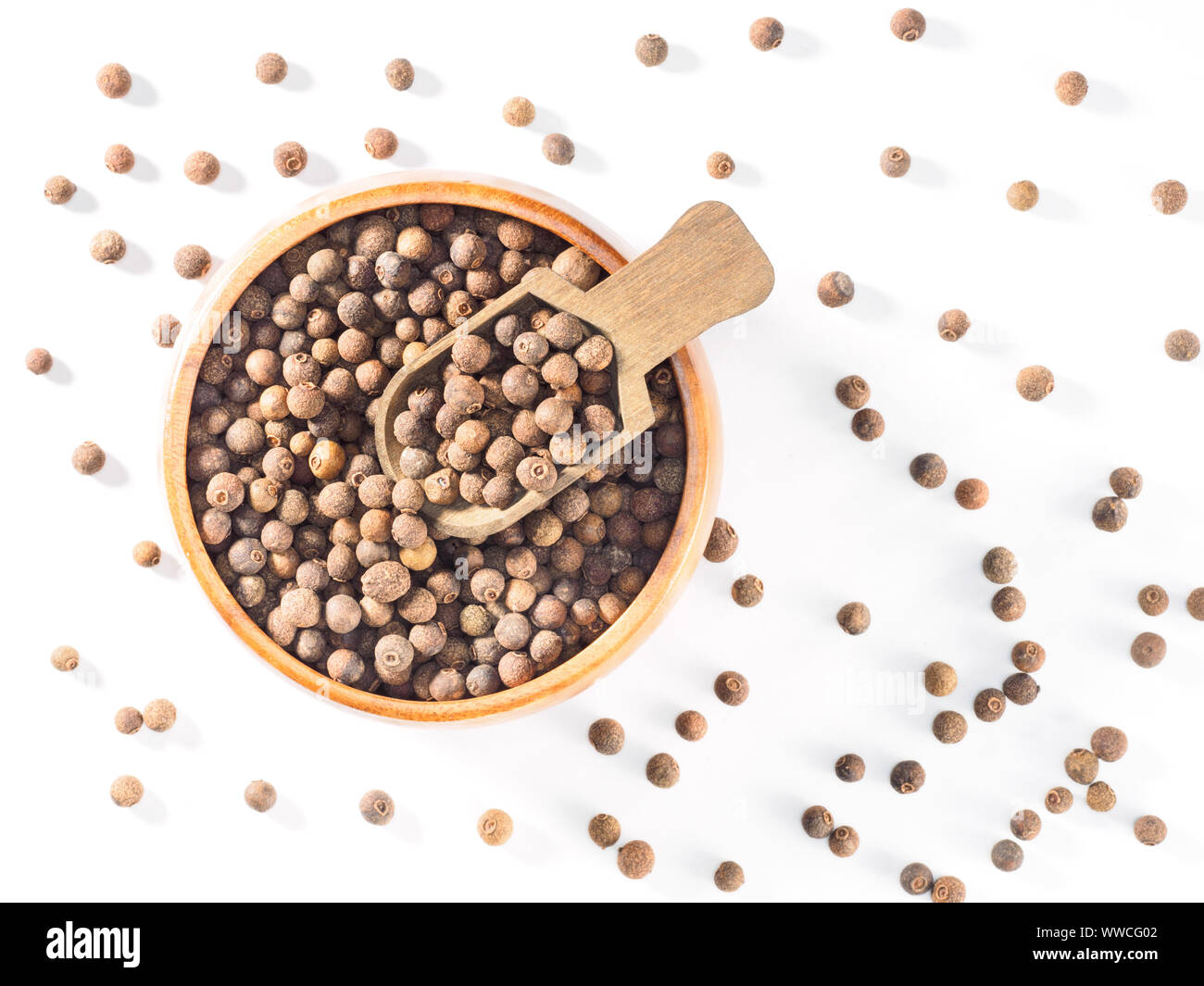 Allspice (Jamaica pepper) in wooden cup and scoop on white background
