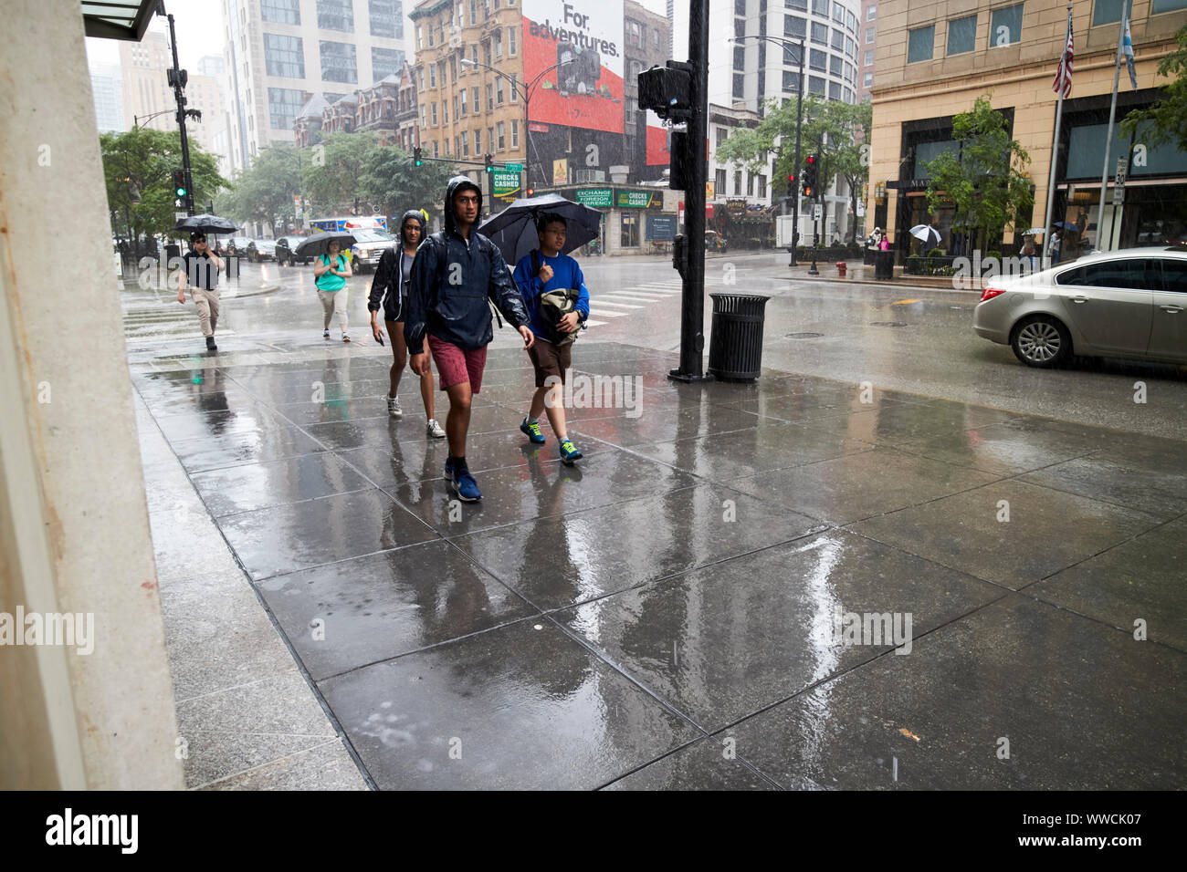 tourists and people walking through torrential rain falling on sidewalk in downtown Chicago Illinois USA Stock Photo