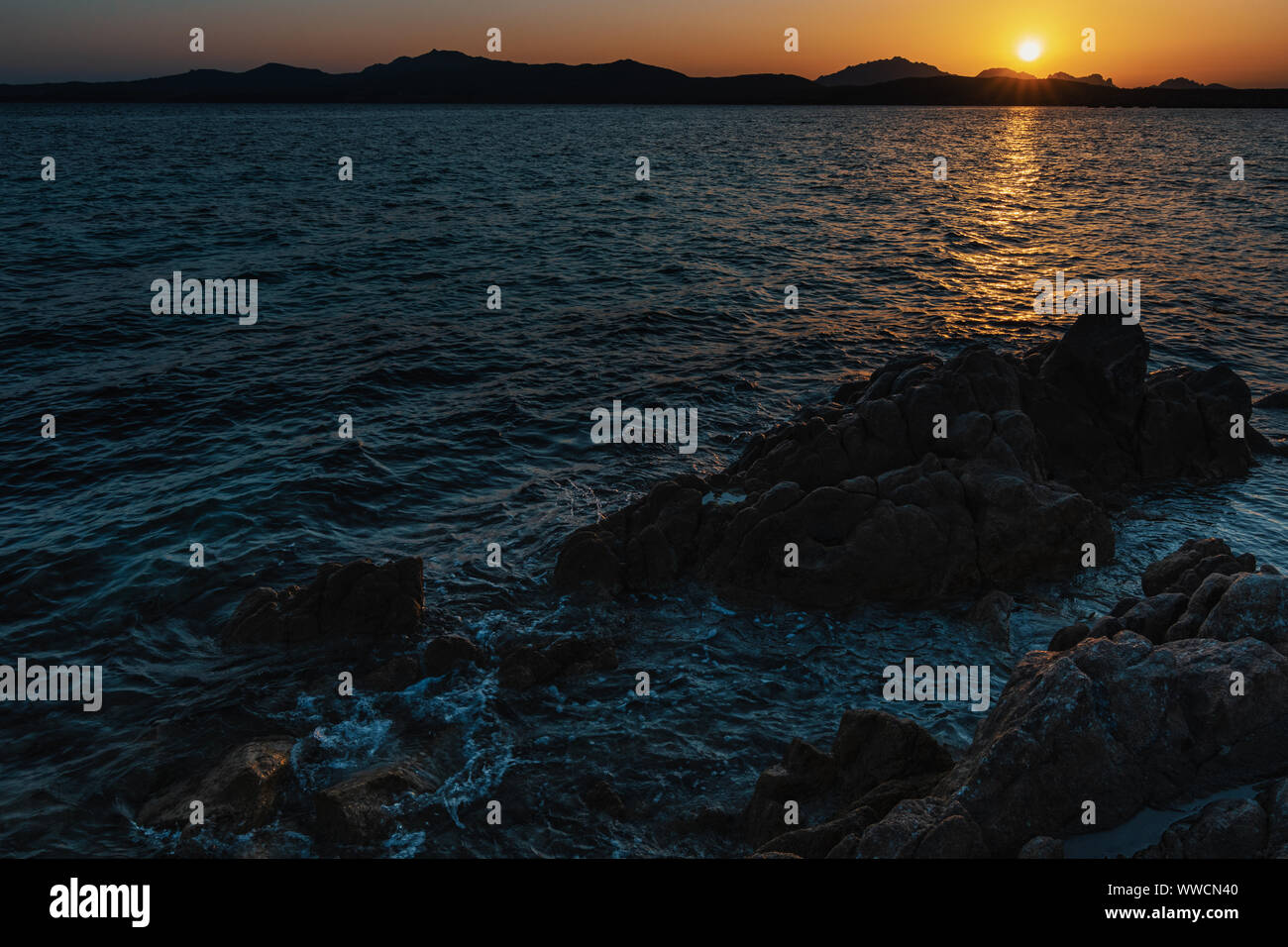 Beautiful mediterranean sunset with sunrays and rocks in the foreground Stock Photo
