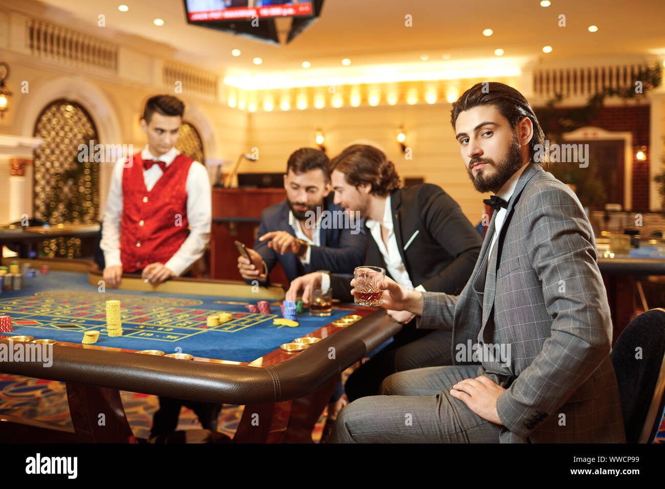 A man in a suit with a glass of whiskey sitting at table roulette playing poker at a casino. Stock Photo
