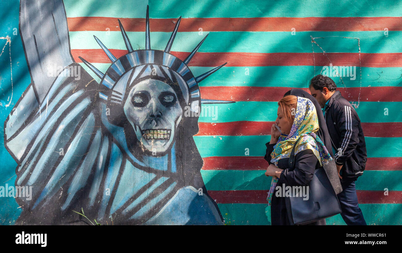 Iranian people walking past a painting of the Statue of Liberty as a skull, in front of the entrance of the former American embassy. Stock Photo