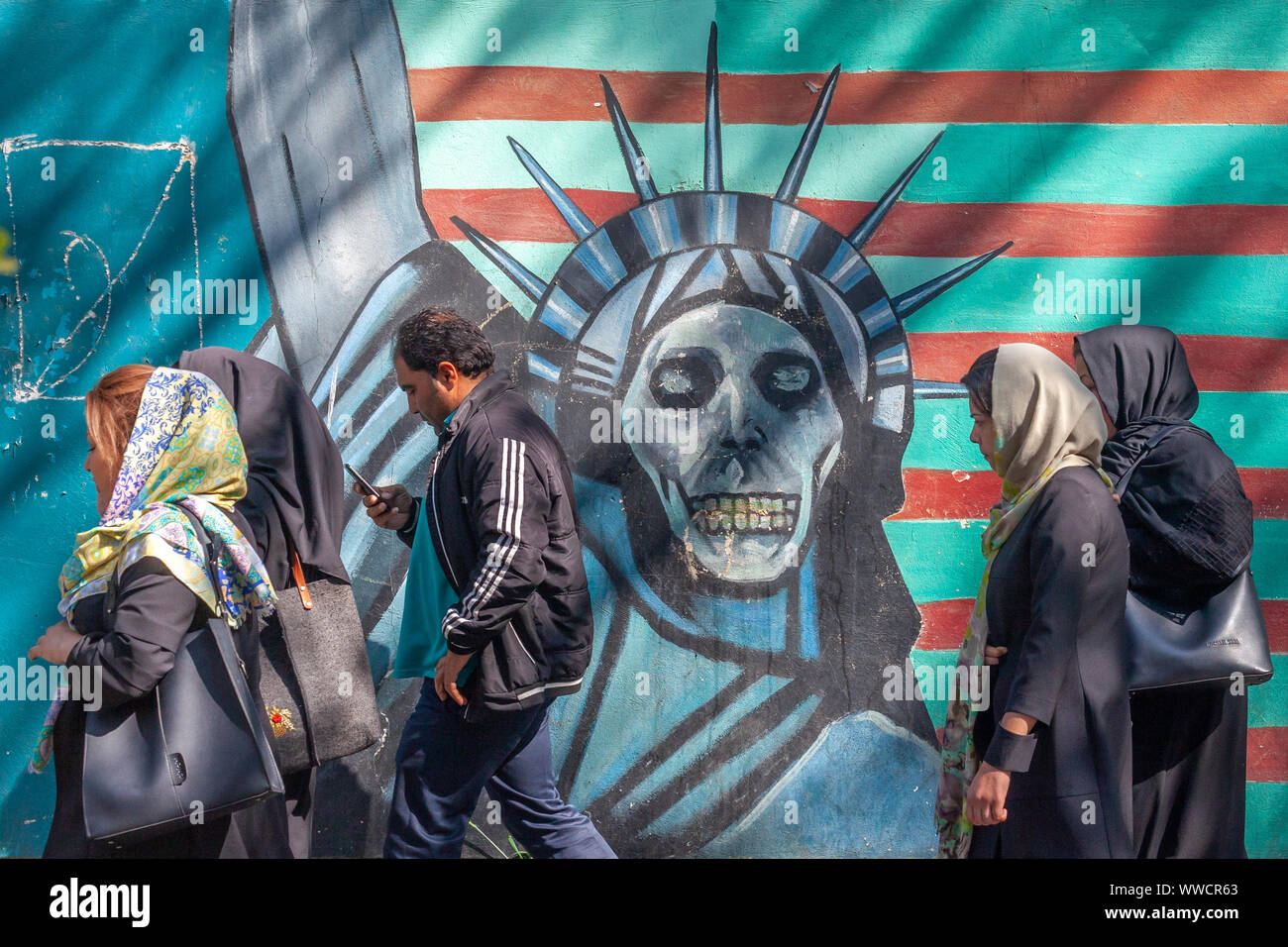 Iranian people walking past a painting of the Statue of Liberty as a skull, in front of the entrance of the former American embassy. Stock Photo