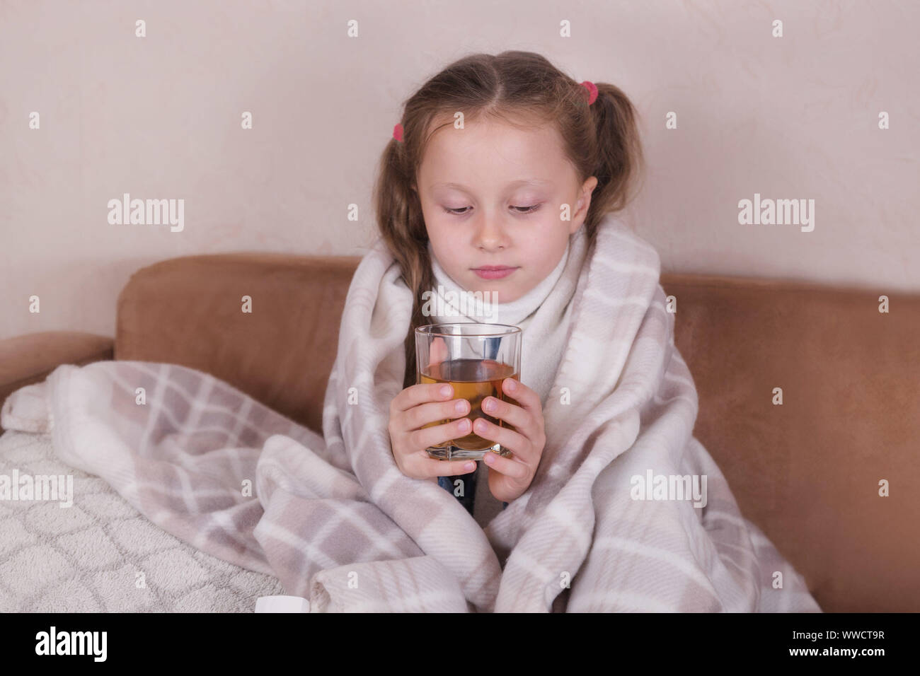 Child taking medicine. Sick girl with scarf lying on bed Stock Photo